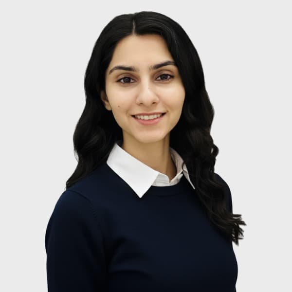 A young woman with long, wavy dark hair smiles at the camera. She is wearing a white collared shirt under a dark navy sweater, standing against a plain light background—perfect for an IT staffing agency in Toronto profile photo.