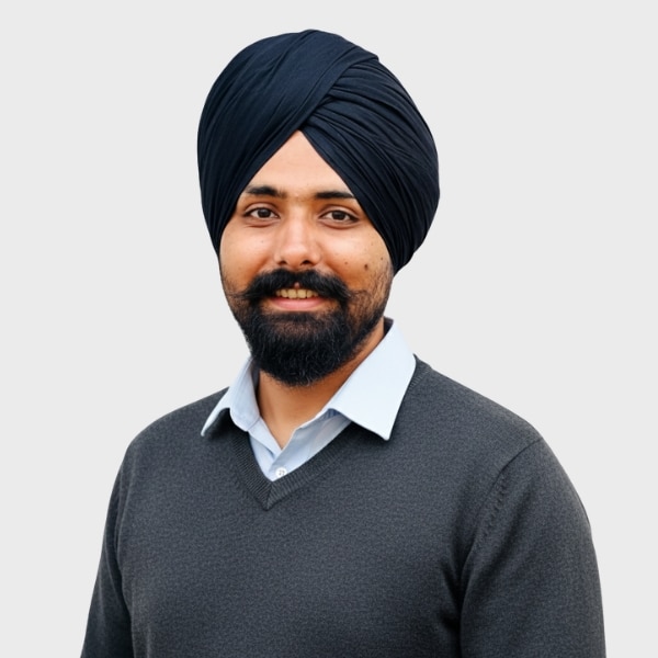 A man with a black turban and beard is smiling. He is wearing a light blue shirt under a dark gray sweater, posed against a plain light gray background, representing an IT staffing agency in Toronto.