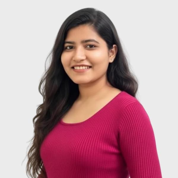 A woman with long, wavy dark hair is smiling and wearing a bright pink ribbed top, representing an IT staffing agency in Toronto. She is standing against a plain light gray background.