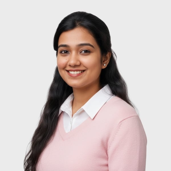 A young woman with long, dark hair smiles at the camera. She is wearing a white collared shirt under a light pink sweater, ready for her new role at an IT staffing agency in Toronto, against a plain, light gray background.