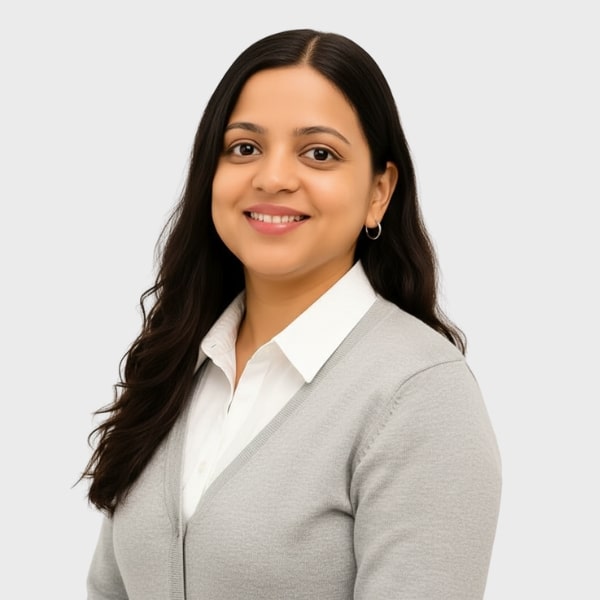 A woman with long dark hair, wearing a light gray sweater over a white collared shirt, smiles while facing slightly to the side against a plain light background—perfect for an IT staffing agency in Toronto profile.