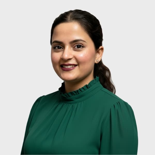 A woman with dark hair pulled back, wearing a green high-neck blouse, smiles at the camera against a plain, light gray background, representing an IT staffing agency in Toronto.