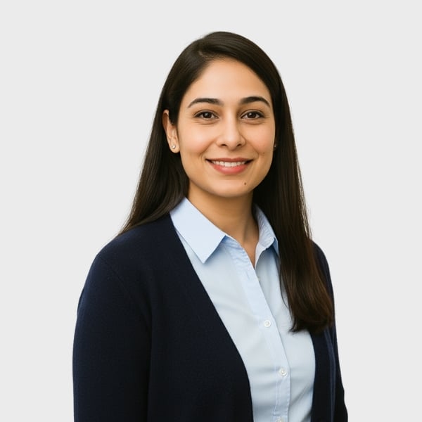 A woman with long dark hair, wearing a light blue button-up shirt and a dark cardigan, smiles at the camera against a plain light background, reflecting the approachable professionalism of an IT staffing agency in Toronto.