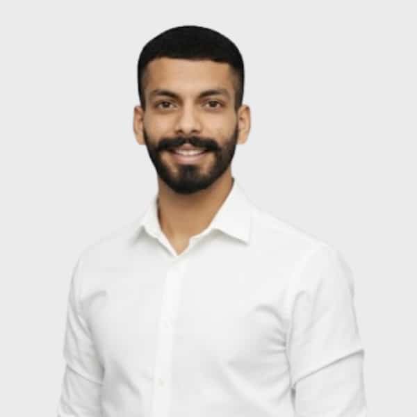 A man with short black hair, a beard, and mustache is smiling and wearing a white button-up shirt against a plain light gray background, representing an IT staffing agency in Toronto.