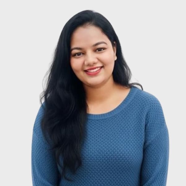 A woman with long black hair wearing a textured blue sweater smiles while standing against a plain light gray background, representing an IT staffing agency in Toronto.