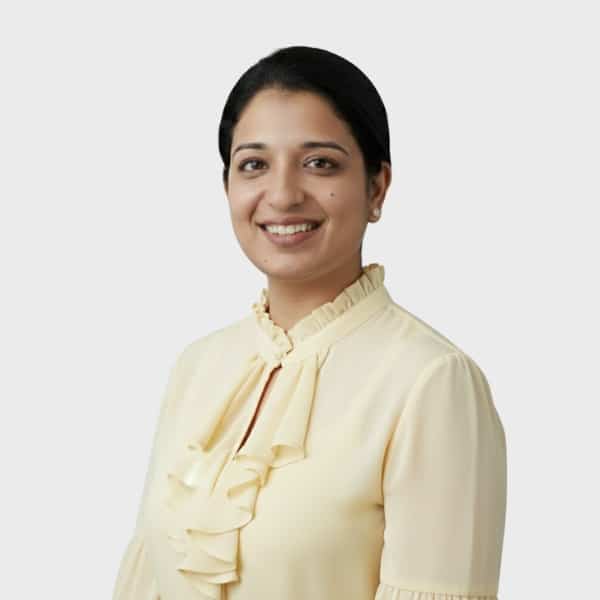 A woman with dark hair tied back, wearing a light yellow blouse with ruffles, smiles at the camera against a plain light gray background, representing a professional from an IT staffing agency in Toronto.