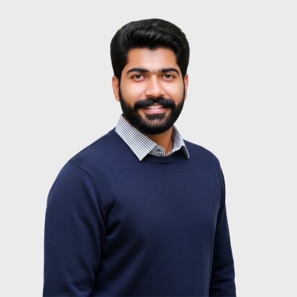 A man with dark hair and a beard, wearing a navy blue sweater over a checkered shirt, smiles at the camera against a plain light gray background—perfect for an IT staffing agency in Toronto.