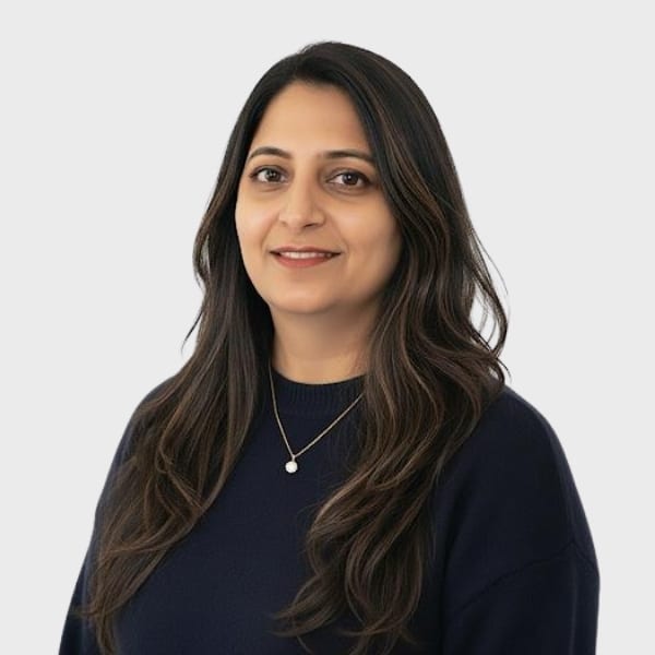 A woman with long, wavy dark hair wearing a dark sweater and a simple necklace smiles gently at the camera, representing an IT staffing agency in Toronto against a light gray background.