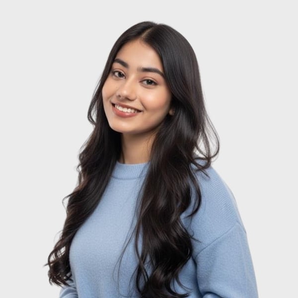 A young woman with long, wavy dark hair wearing a light blue sweater smiles softly at the camera against a plain light background, presenting a friendly face for an IT staffing agency in Toronto.
