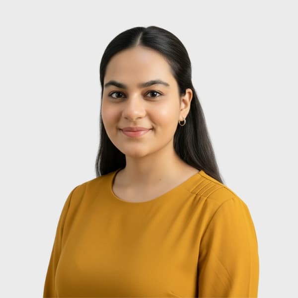 A woman with long dark hair, wearing a mustard yellow top, smiles gently while looking at the camera against a plain light gray background, reflecting the professional yet approachable image of an IT staffing agency in Toronto.
