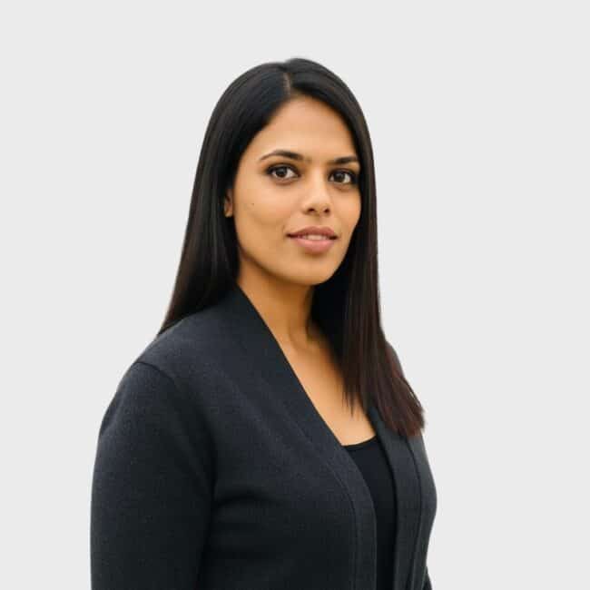 A woman with straight, dark hair wearing a black top and blazer stands against a plain light gray background, looking confidently at the camera—ideal for representing an IT staffing agency in Toronto.