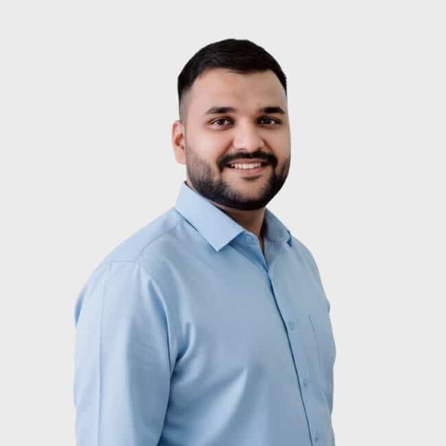 A man with short dark hair and a beard, wearing a light blue button-up shirt, smiles at the camera against a plain white background—perfect for an IT staffing agency in Toronto.